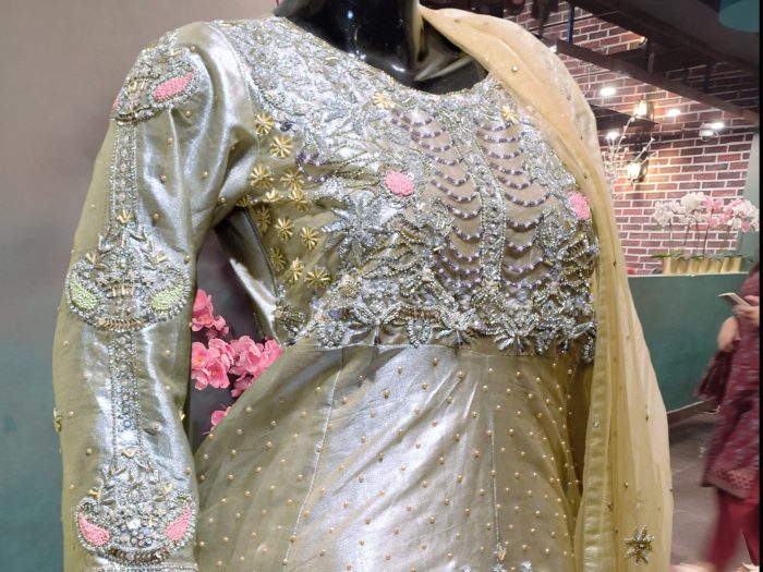 A detailed close-up of "Champaign Artistry," highlighting the exquisite silver hand embellishments on the champagne gold fabric. The delicate craftsmanship and intricate detailing add a luxurious touch to this elegant ensemble.