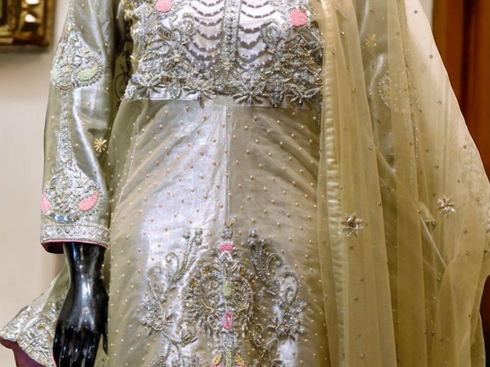 Champaign Artistry" – A champagne gold peplum dress adorned with intricate silver hand embellishments. Paired with raw silk pants and a delicate net dupatta, this ensemble radiates grace and sophistication.